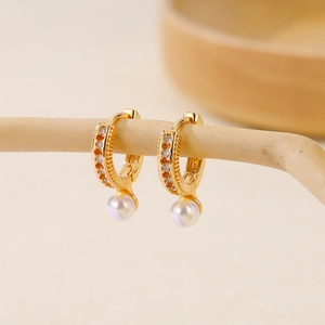 Gold plated pearl drop earrings with zircon crystals on a minimalist wooden display