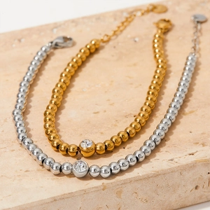 Polished gold and silver beaded bracelets with crystal pendants on beige stone slab