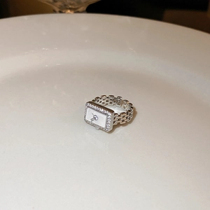 Macro shot of silver clock-shaped ring with zircon inlay placed on white ceramic dish