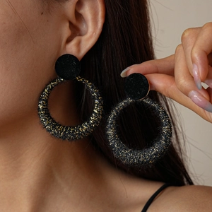 Elegant black flocked round earrings with gold glitter finish worn by a model