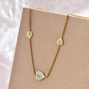 Gold titanium steel box chain necklace with three hollow leaf pendants on a tan background