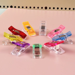 Set of colorful plastic sewing clips with metal springs arranged on a pink background