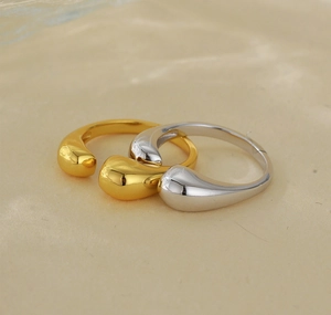 Close-up of gold and silver teardrop rings with polished geometric finish on neutral background