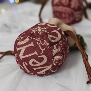 Close-up of burgundy Christmas drawstring gift bag with Merry Christmas print and satin ribbons