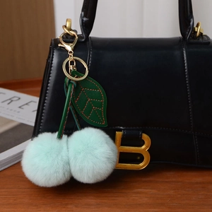 Detail of light green cherry plush keychain hanging on a black textured handbag with gold clasp