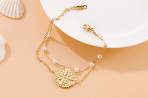 Detail of gold double-layered stainless steel bracelet with white pearl and star coin charm