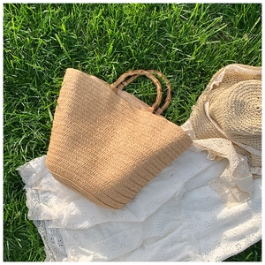 Detail of summer straw tote bag featuring natural bamboo handles on white lace and grass