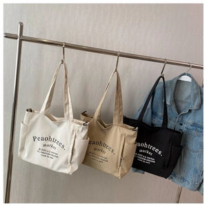 Detailed shot of three canvas tote bags in beige, khaki and black with shoulder straps