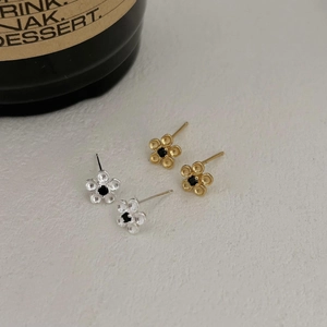 Close-up of minimalist matte flower stud earrings with black center stone in gold and silver