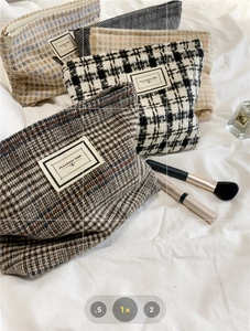 Close-up of checkered tweed cosmetic bags on white fabric with perfume and brushes
