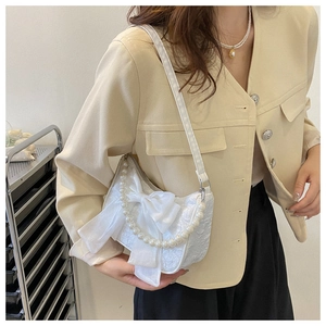 Detailed view of white lace fabric handbag with a satin bow and pearl shoulder strap