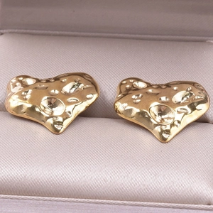 Macro detail of gold heart stud earrings featuring unique hammered metal texture and finish