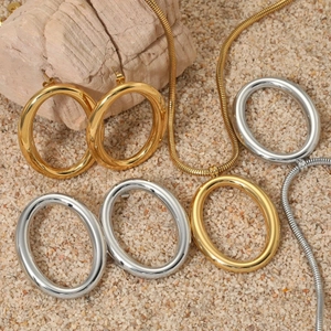 Minimalist gold and silver oval pendant necklaces and earrings set on sand