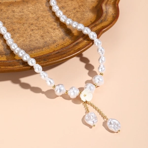 Detail of baroque pearl necklace featuring a white floral motif and gold tassel charms