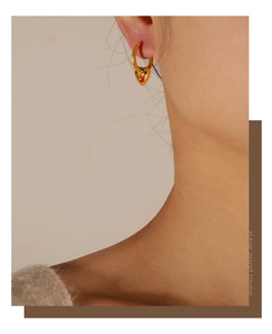 Macro view of gold hoop earrings with red and green enamel heart pendants on model