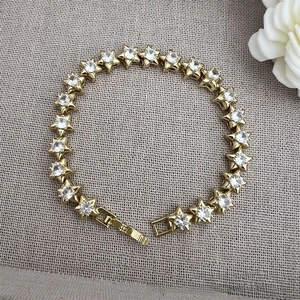 Macro detail of star-shaped gold bracelet with zircon stones on grey fabric background