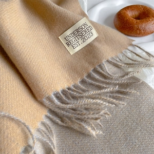 Detailed texture of beige cashmere scarf featuring elegant fringe and brand woven label