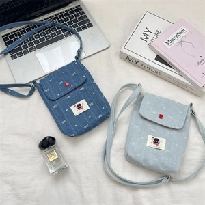 Detail van kleine denim crossbody tassen met witte strikken en rode drukknopen