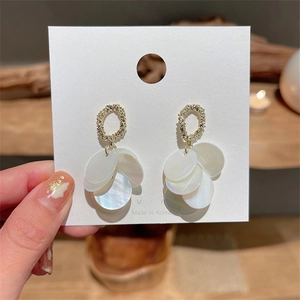 Macro detail of gold-tone earrings featuring white resin discs and textured finish