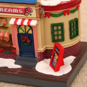 Close-up of a miniature glowing ice cream shop music box with festive snow details