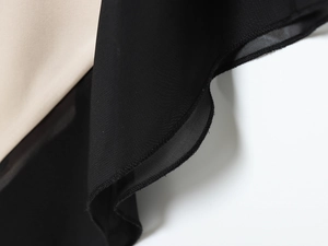 Detailaufnahme des Satin-Kleides mit zweifarbigen Nähten in Schwarz und Beige am Saum