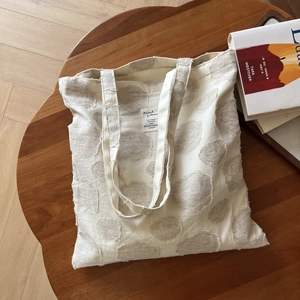 Detail shot of the textured beige cotton tote bag with a cloud pattern on a wooden table