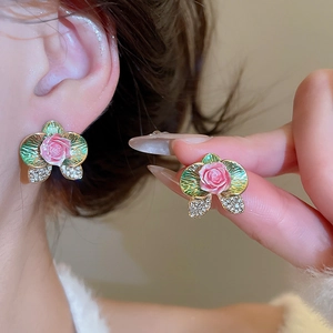 Detailed view of flower earrings with pink roses, green leaves and sparkling crystals