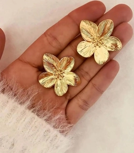 Detail showing oversized gold five-petal flower earring with polished metal finish