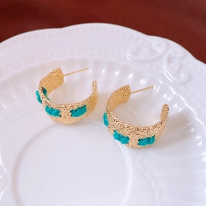 Detail of C-shaped vintage earrings with hammered gold metal and blue knit texture