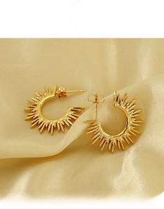 Macro view of gold sunburst fan earrings in durable titanium steel on silk background