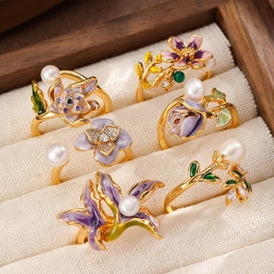 Detailed close-up of floral enamel rings with pearls in a wooden jewelry display box