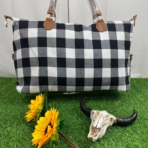 Detail of checkered weekender bag with brown leather handles on green grass background