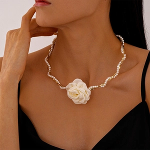 Close-up of elegant fabric camellia flower with pearl and gold metal twisted necklace