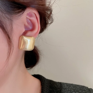 Close-up of golden square earrings with brushed metal finish on model ear