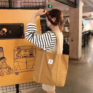 Detail of a ginger yellow corduroy tote bag featuring a white woven label and shoulder straps