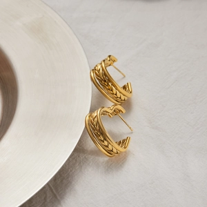 Close-up of golden heart earrings with woven wheat texture on white fabric background