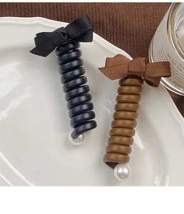 Détail d'élastiques spirales avec nœuds et perles dans un plateau sur tricot marron