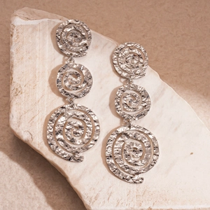 Détail de boucles d'oreilles créoles argentées vintage sur un socle en pierre
