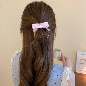 Rear view of a soft pink satin bow hair tie styling a half-up hairstyle in a warm home setting