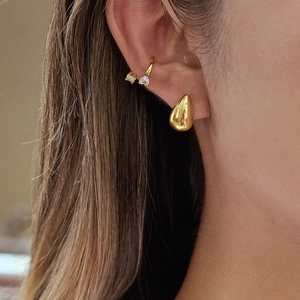 Gros plan sur boucle d'oreille goutte dorée et anneau zircon pour look superposé