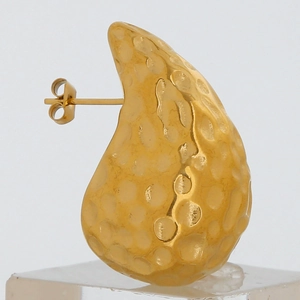 Close-up of golden teardrop earring with hammered metal texture on a clear stand