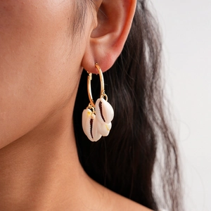 Bohemian gold hoop earrings with white cowrie shell charms on female model