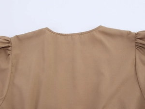 Detail of khaki puff sleeve dress showing the round neckline and pleated shoulder stitching