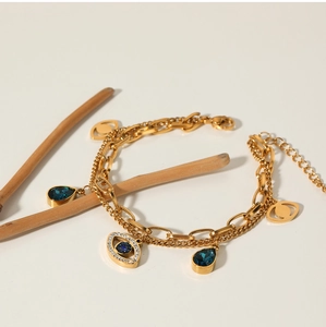 Detail of gold double-layer bracelet with blue teardrop gems and evil eye charms