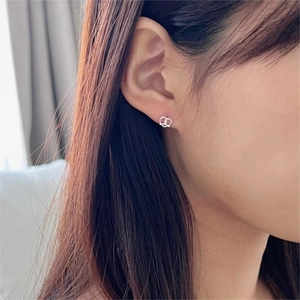 Detail view of 925 silver pretzel heart earrings worn on ear with soft lighting