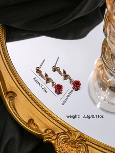 Detail view of red rose earrings with gold metal stems and ruby accents on mirror tray