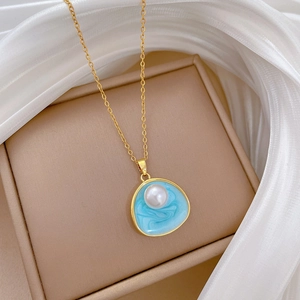 Gros plan d'un collier doré avec émail bleu clair et perle sur un écrin beige