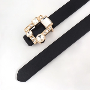 Close-up of a slim black leather belt featuring a luxury gold buckle with clear rhinestones