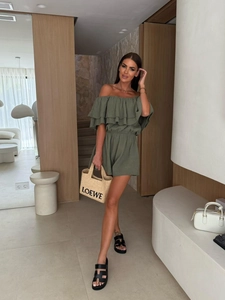 Detail of the ruffle off-shoulder neckline and smocked waist on a dark green romper