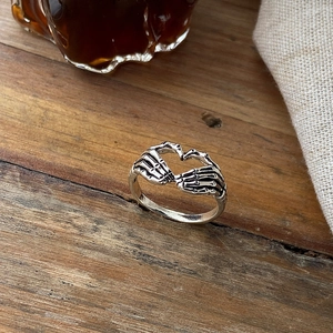 Close-up of vintage silver skeleton hand heart ring on textured wooden background